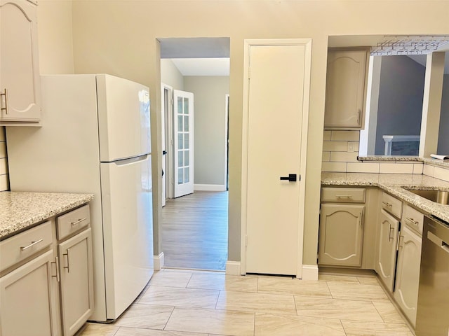 kitchen featuring stainless steel dishwasher, white fridge, light stone countertops, and backsplash