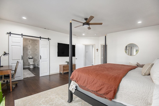 bedroom featuring connected bathroom, ceiling fan, dark wood-type flooring, and a barn door