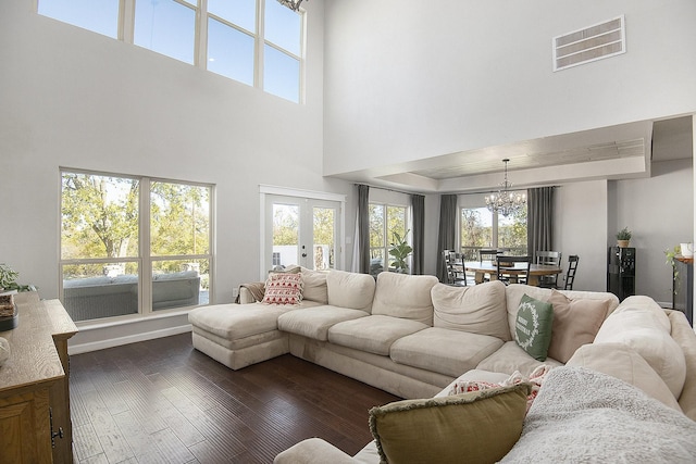 living room with a notable chandelier, dark wood-type flooring, a high ceiling, and french doors