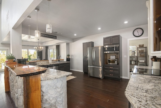 kitchen featuring sink, dark hardwood / wood-style flooring, kitchen peninsula, pendant lighting, and appliances with stainless steel finishes