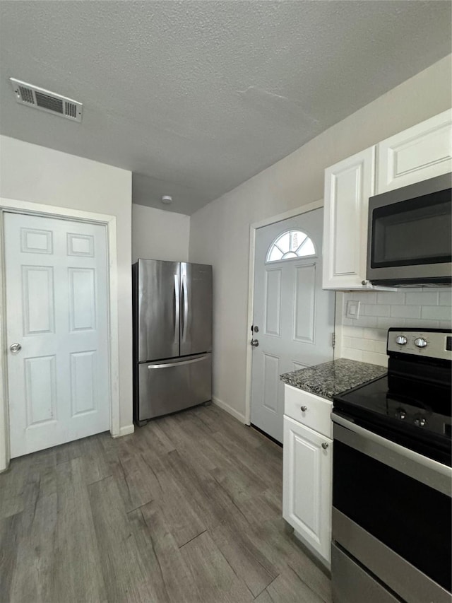 kitchen featuring decorative backsplash, white cabinetry, dark stone countertops, and stainless steel appliances