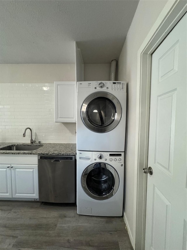 clothes washing area with a textured ceiling, dark hardwood / wood-style floors, stacked washer and clothes dryer, and sink