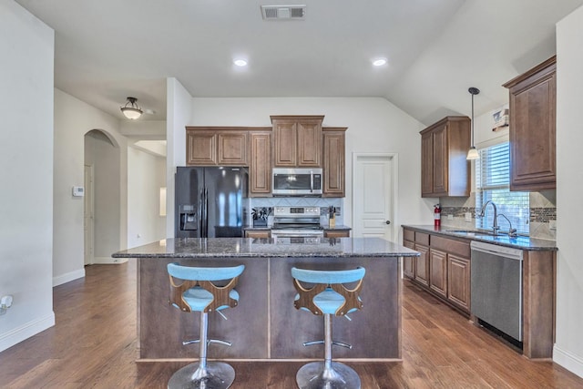 kitchen with dark hardwood / wood-style flooring, dark stone counters, stainless steel appliances, sink, and a kitchen island