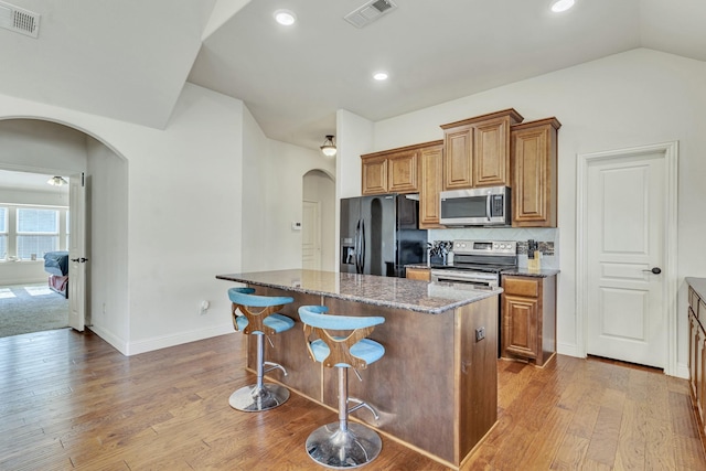 kitchen with dark stone counters, stainless steel appliances, hardwood / wood-style flooring, a center island, and lofted ceiling