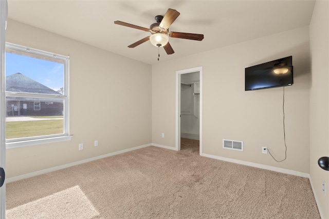 unfurnished bedroom with ceiling fan, a walk in closet, a closet, and light carpet