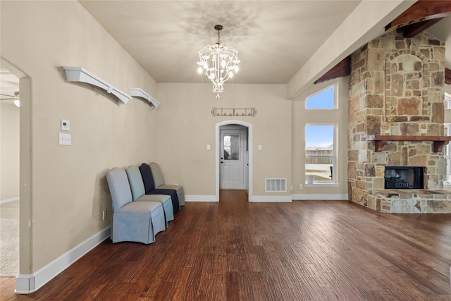 unfurnished room with a stone fireplace, ceiling fan with notable chandelier, and dark hardwood / wood-style flooring