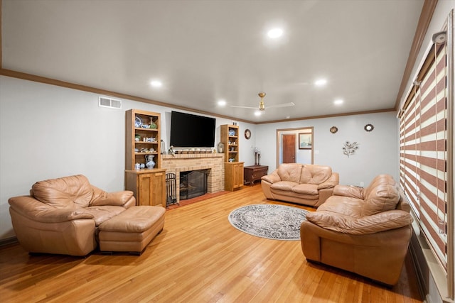 living room with crown molding, a brick fireplace, visible vents, and light wood-style flooring
