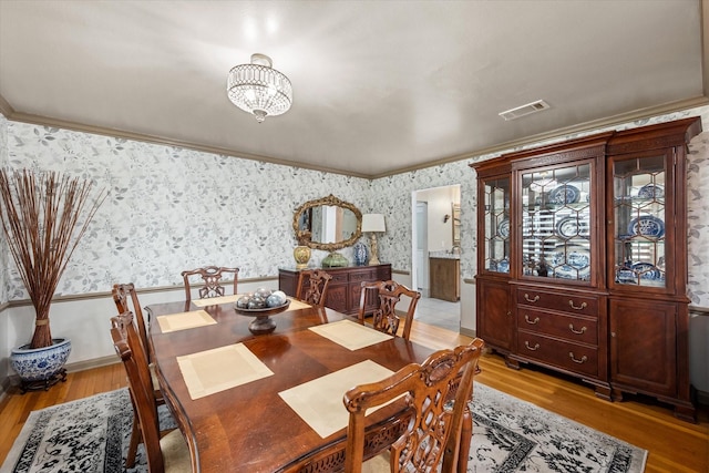 dining area featuring ornamental molding, light wood-type flooring, and a notable chandelier