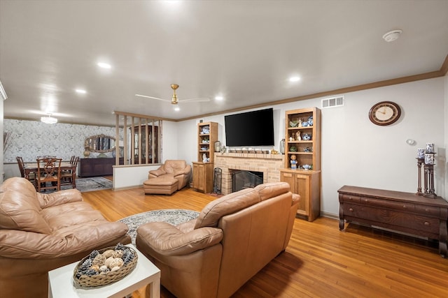 living area featuring wallpapered walls, wood finished floors, visible vents, a brick fireplace, and ceiling fan