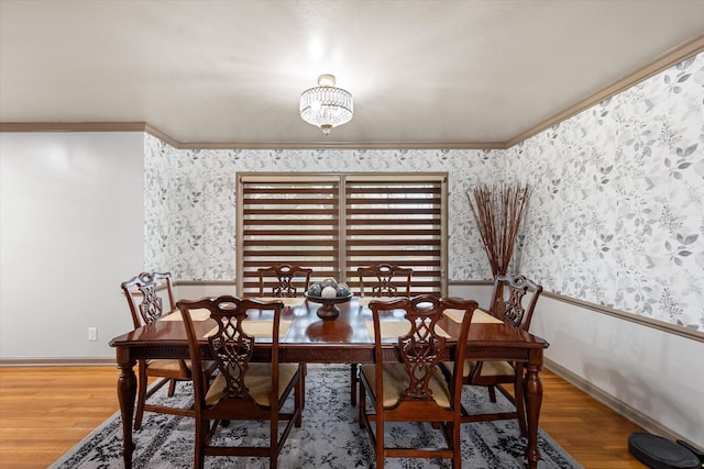 dining room featuring wallpapered walls, wood finished floors, baseboards, and ornamental molding