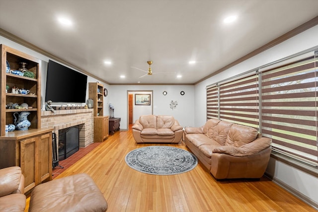 living room with a brick fireplace, ceiling fan, crown molding, and light hardwood / wood-style flooring