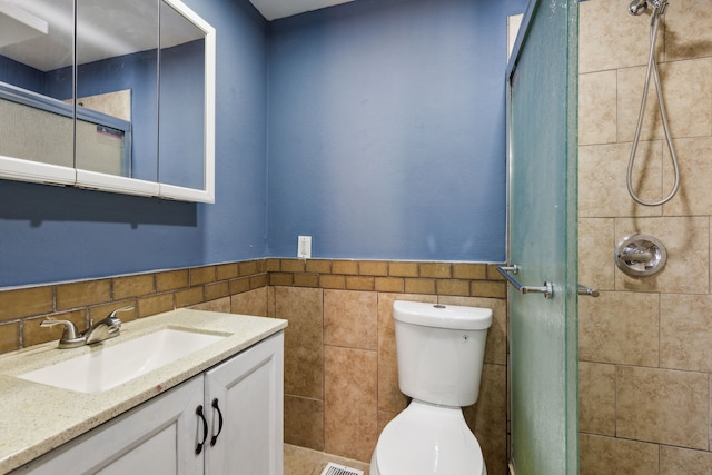 bathroom with a tile shower, vanity, tile walls, and toilet