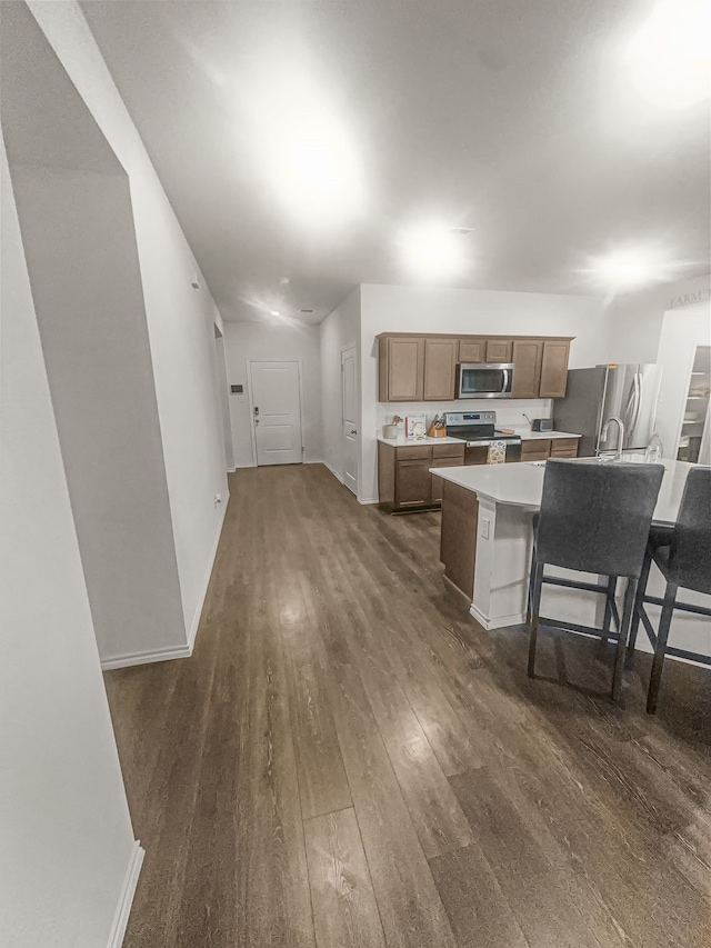 kitchen with appliances with stainless steel finishes, a kitchen island with sink, a breakfast bar area, and dark hardwood / wood-style flooring