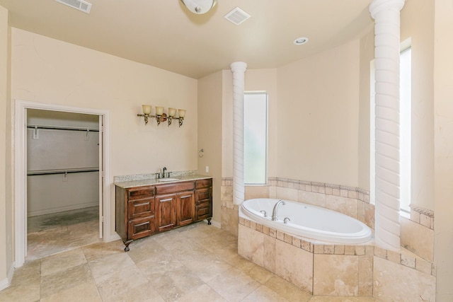 bathroom with decorative columns, tiled bath, and vanity