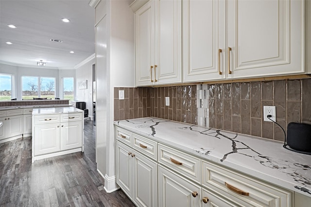 kitchen with tasteful backsplash, white cabinetry, dark hardwood / wood-style flooring, ornamental molding, and light stone countertops