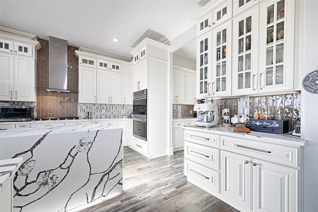 kitchen with white cabinetry, decorative backsplash, wall chimney exhaust hood, stainless steel appliances, and light hardwood / wood-style flooring