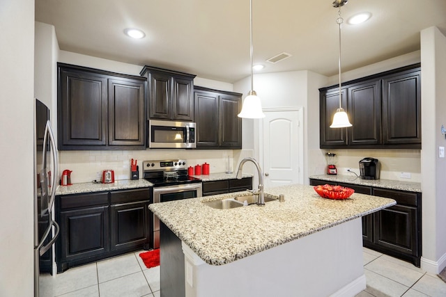 kitchen featuring light stone countertops, stainless steel appliances, a kitchen island with sink, sink, and decorative light fixtures