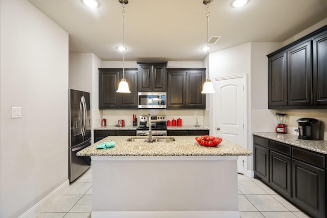 kitchen featuring light stone countertops, sink, an island with sink, decorative light fixtures, and appliances with stainless steel finishes