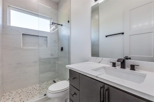 bathroom with decorative backsplash, a tile shower, vanity, and toilet