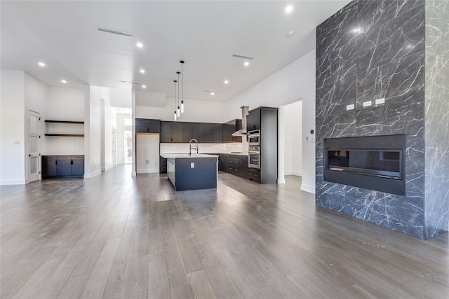 kitchen featuring dark wood-type flooring, sink, an island with sink, hanging light fixtures, and a tiled fireplace