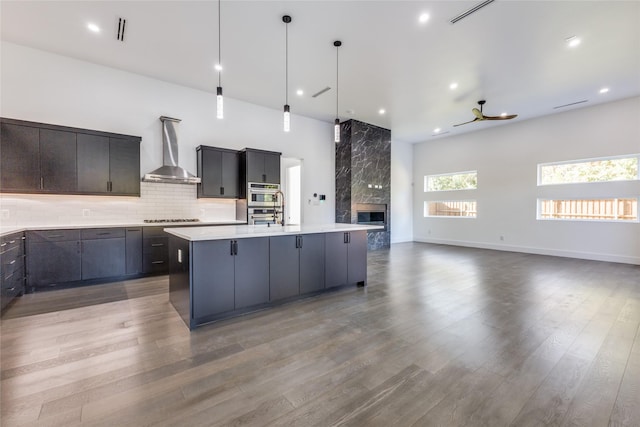 kitchen featuring wall chimney exhaust hood, wood-type flooring, a kitchen island with sink, and decorative light fixtures