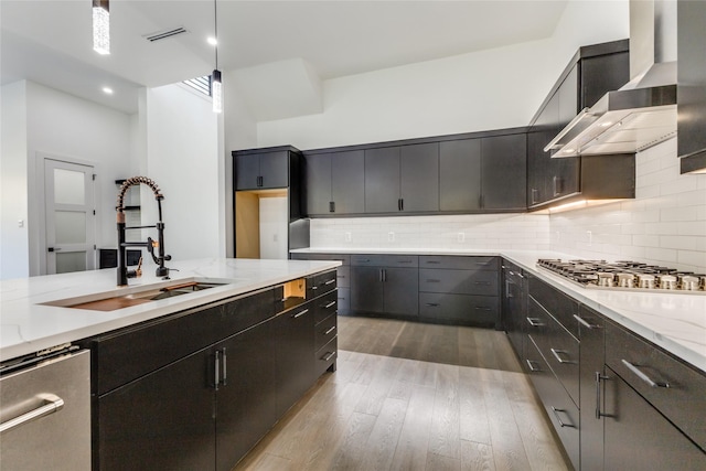 kitchen featuring wall chimney exhaust hood, sink, decorative light fixtures, light hardwood / wood-style flooring, and appliances with stainless steel finishes