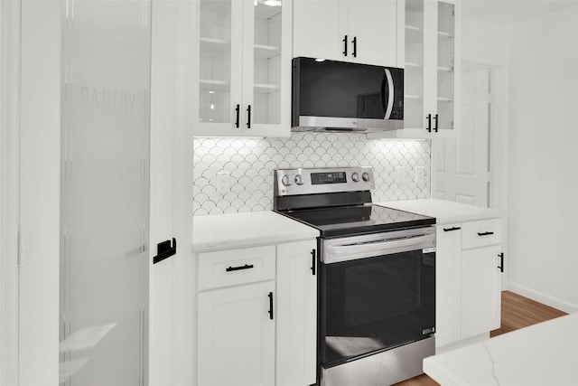 kitchen with backsplash, white cabinets, light wood-type flooring, light stone counters, and stainless steel electric range