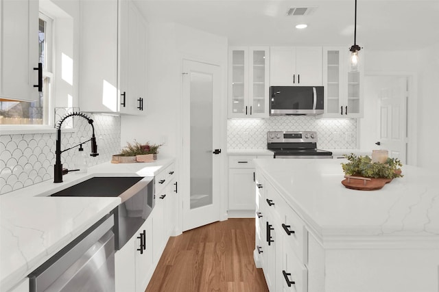 kitchen featuring white cabinets, tasteful backsplash, hanging light fixtures, and appliances with stainless steel finishes