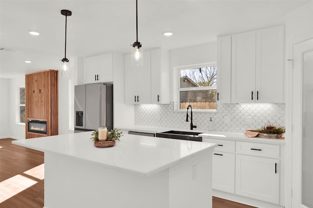 kitchen featuring stainless steel refrigerator with ice dispenser, hanging light fixtures, white cabinetry, light stone countertops, and a kitchen island