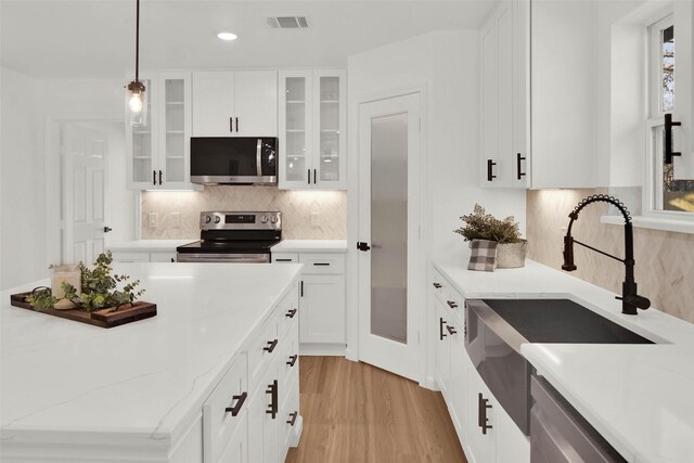 kitchen featuring pendant lighting, sink, white cabinets, light stone counters, and stainless steel appliances