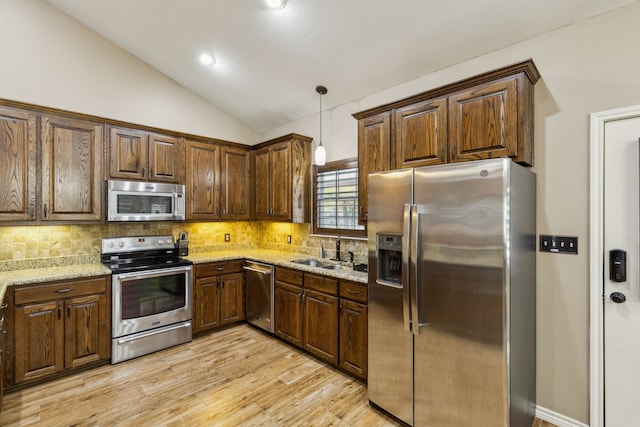 kitchen featuring lofted ceiling, sink, appliances with stainless steel finishes, pendant lighting, and light stone countertops