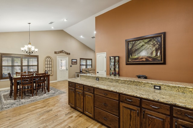 kitchen featuring pendant lighting, a chandelier, dark brown cabinetry, light stone counters, and light hardwood / wood-style floors