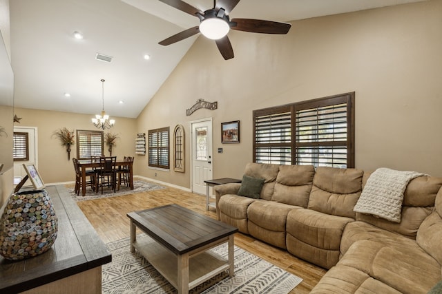 living room with ceiling fan with notable chandelier, high vaulted ceiling, and light hardwood / wood-style flooring