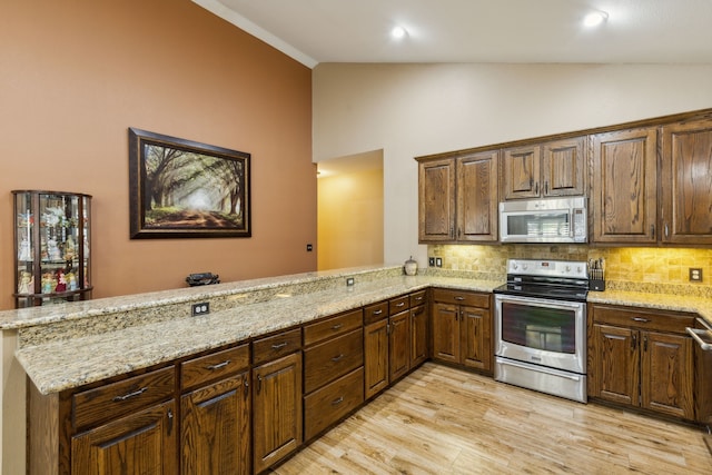 kitchen with light stone countertops, appliances with stainless steel finishes, lofted ceiling, and kitchen peninsula