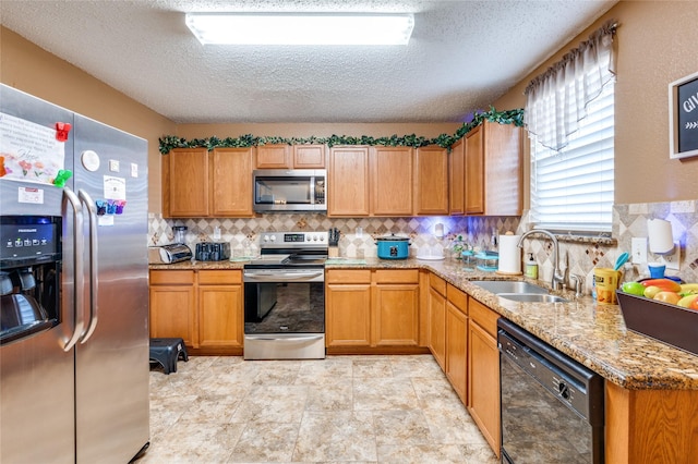 kitchen with stainless steel appliances, brown cabinetry, a sink, and light stone countertops