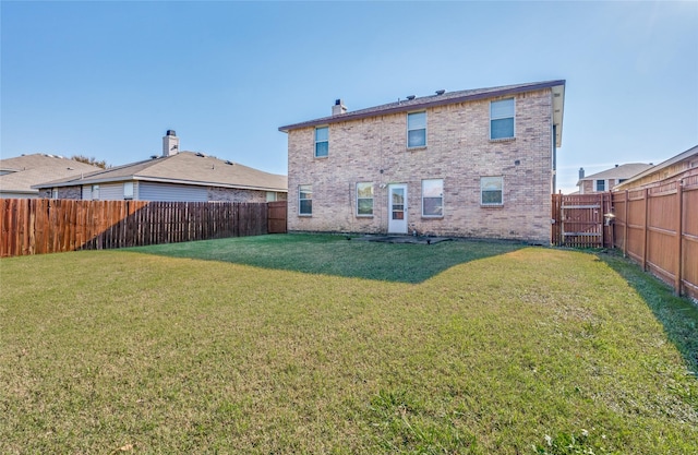 rear view of house featuring a fenced backyard, brick siding, a chimney, and a lawn