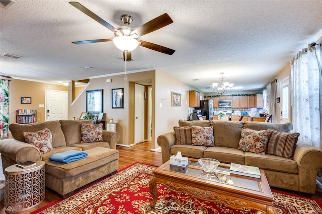 living room featuring a textured ceiling, ceiling fan with notable chandelier, visible vents, light wood-style floors, and crown molding