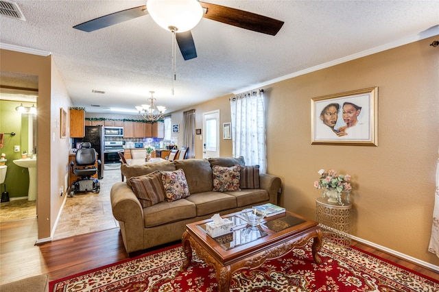 living room with crown molding, visible vents, light wood-style floors, a textured ceiling, and ceiling fan with notable chandelier