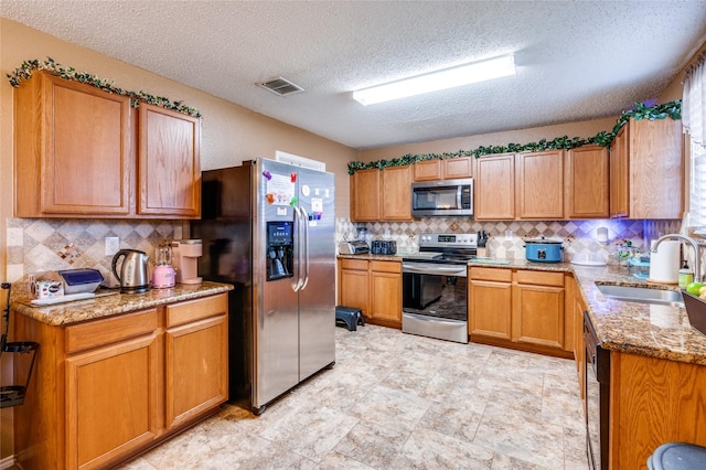 kitchen featuring decorative backsplash, light stone counters, brown cabinets, stainless steel appliances, and a sink