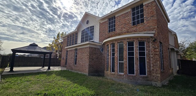 rear view of house featuring a gazebo, a lawn, and a patio