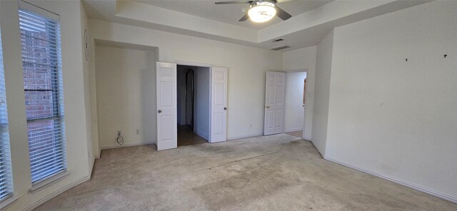 unfurnished bedroom with light carpet, a tray ceiling, and ceiling fan