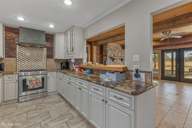 kitchen featuring white cabinetry, wall chimney range hood, dark stone countertops, and stainless steel gas stove