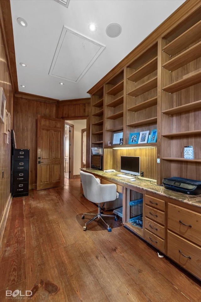 office with dark hardwood / wood-style flooring, built in desk, ornamental molding, and wooden walls