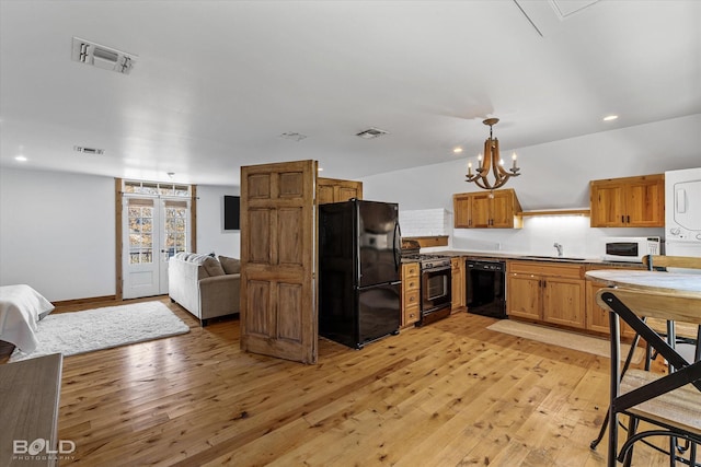 kitchen with stacked washing maching and dryer, light wood-type flooring, hanging light fixtures, and black appliances