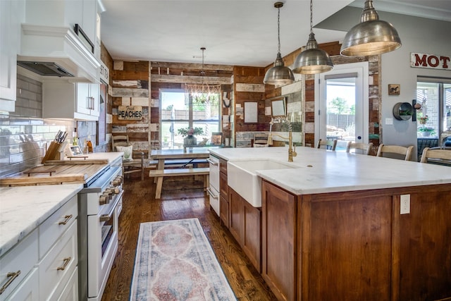 kitchen with decorative light fixtures, high end range oven, white cabinetry, and a kitchen island with sink