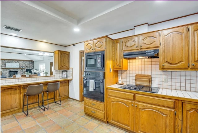 kitchen featuring black appliances, tile counters, a breakfast bar, and tasteful backsplash