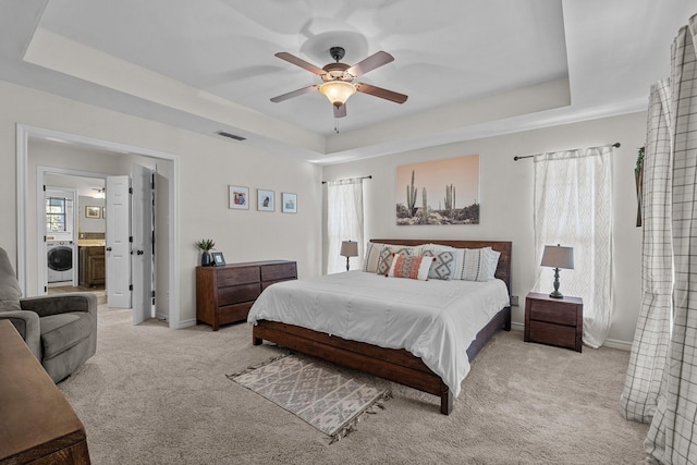 carpeted bedroom featuring washer / dryer, connected bathroom, a tray ceiling, and ceiling fan