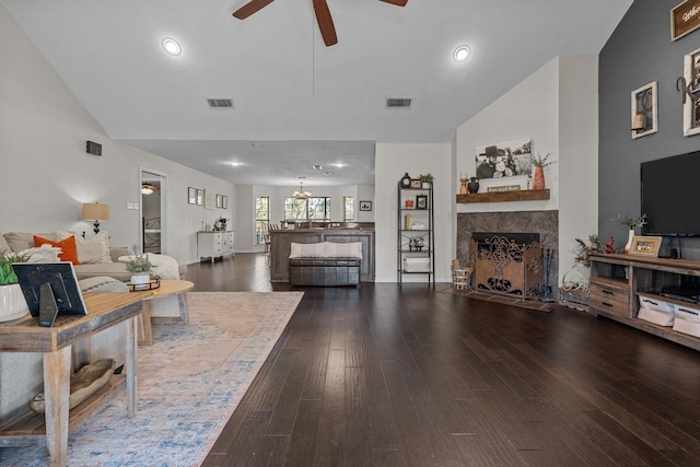 living room with a tiled fireplace, ceiling fan with notable chandelier, dark wood-type flooring, and vaulted ceiling