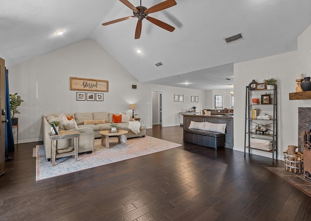 living room with high vaulted ceiling, dark hardwood / wood-style floors, a stone fireplace, and ceiling fan