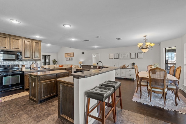 kitchen with a kitchen island with sink, dark wood-type flooring, black appliances, decorative light fixtures, and a notable chandelier